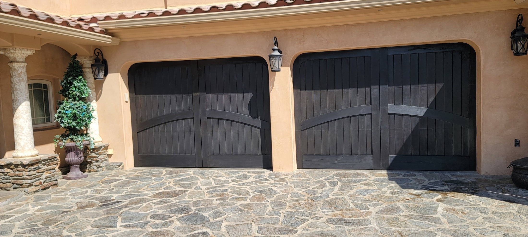 Custom black garage doors with stone driveway and stucco exterior.